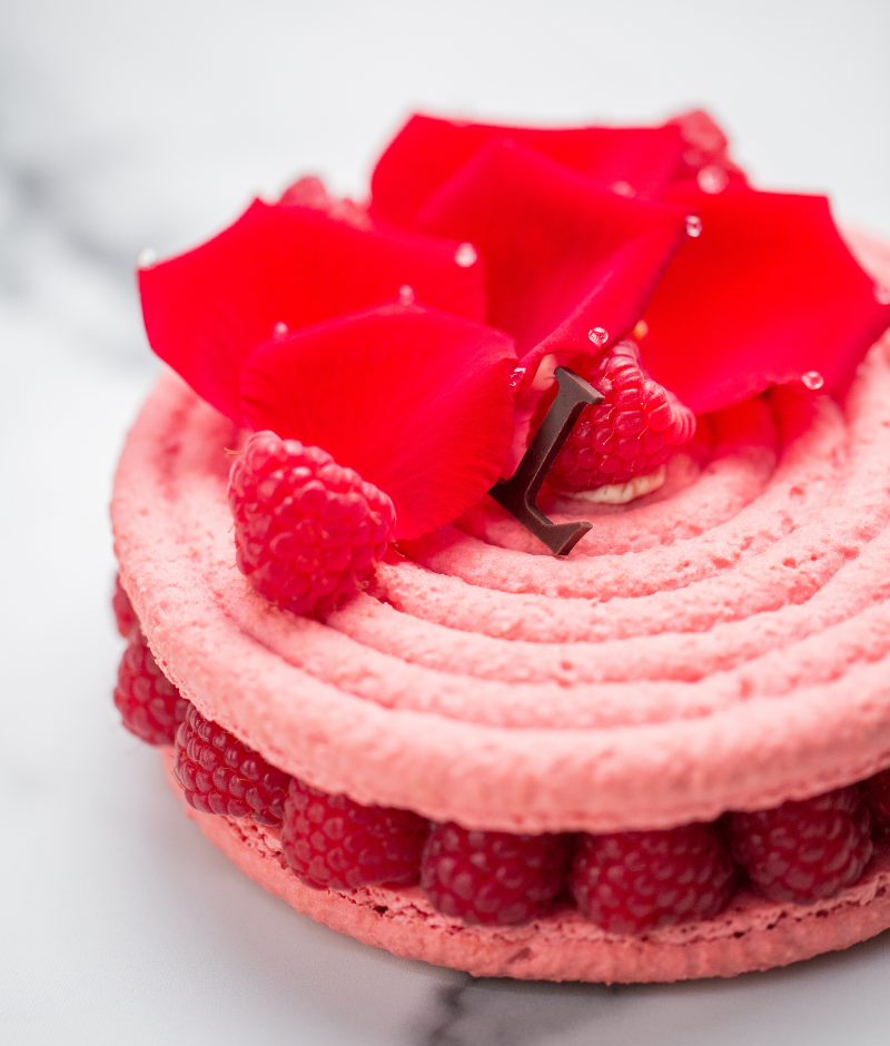 Rose macaron topped with a smooth cream scented with rose petals and lychees, garnished with fresh raspberries.