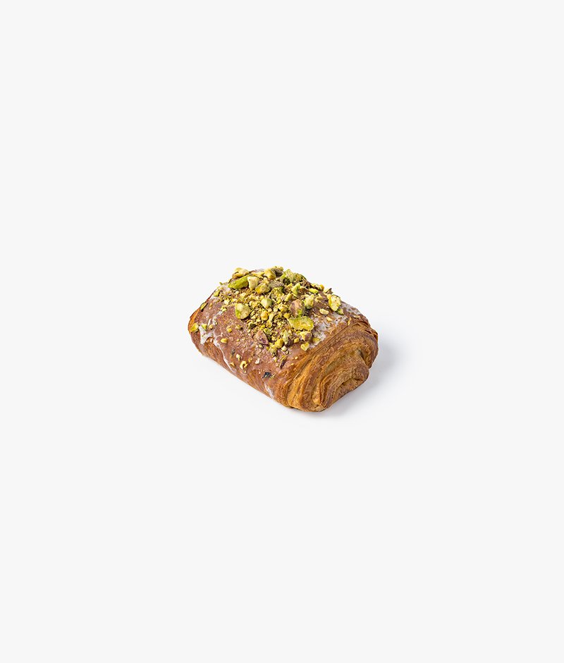 The signature pistachio pain au chocolat: a puff pastry filled with pistachio paste and two chocolate bars, decorated with a sugar glaze and pistachio chips. All viennoiserie is served with a small napkin.