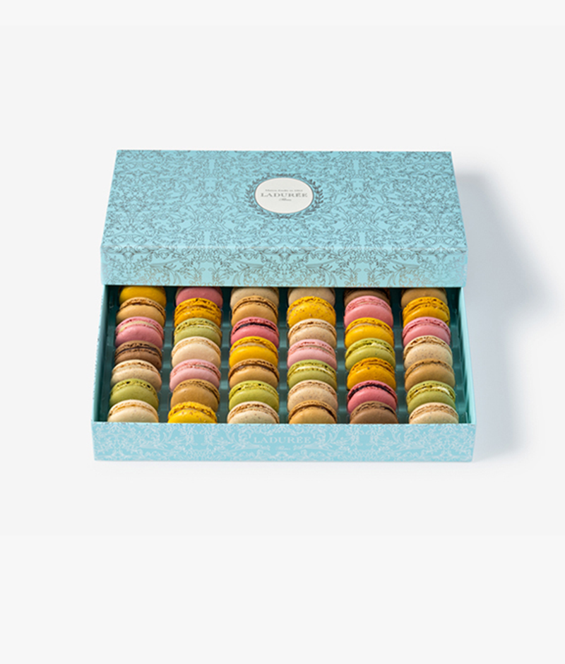 La Maison Ladurée's signature "Arabesque" motif is featured on a box of 42 macarons in a silver version on a blue background.