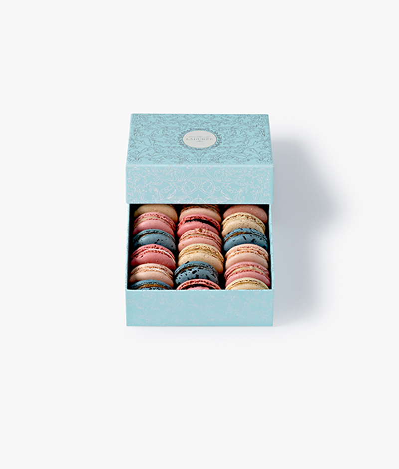 La Maison Ladurée's signature "Arabesque" motif is featured on a box of 18 macarons in a silver version on a blue background.